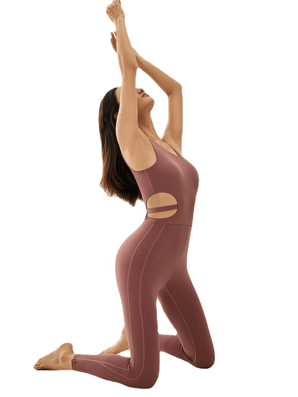 Woman wearing a sports elastic one-piece sleeveless yoga jumpsuit in camel color, kneeling with arms raised, showcasing flexibility in pose.